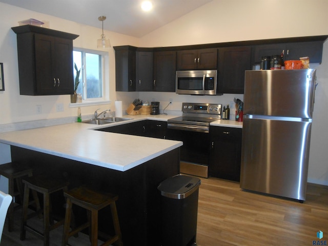 kitchen featuring pendant lighting, lofted ceiling, sink, appliances with stainless steel finishes, and light hardwood / wood-style floors