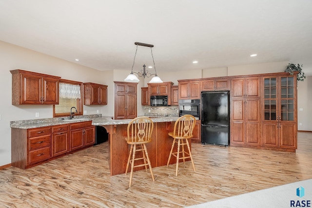 kitchen with a center island, black appliances, sink, light hardwood / wood-style flooring, and light stone countertops