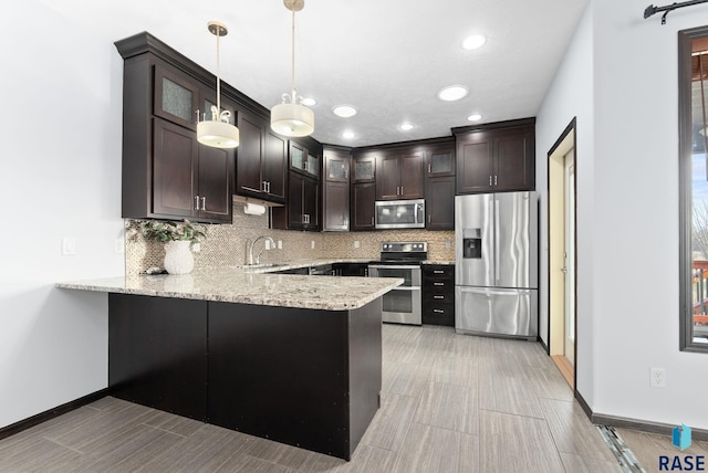 kitchen with hanging light fixtures, decorative backsplash, appliances with stainless steel finishes, dark brown cabinets, and kitchen peninsula