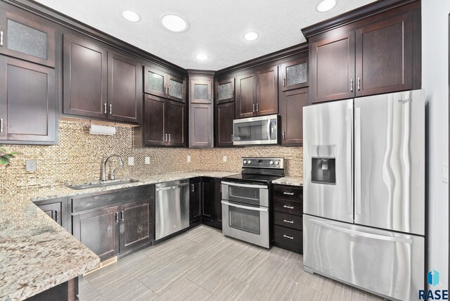 kitchen with appliances with stainless steel finishes, light stone counters, dark brown cabinets, and sink