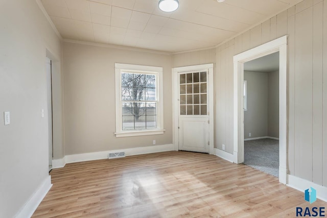 spare room featuring wood walls, crown molding, and light hardwood / wood-style flooring