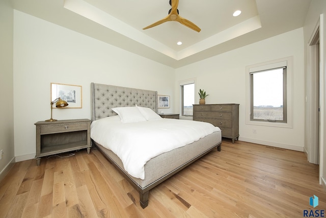 bedroom with a raised ceiling, ceiling fan, and light hardwood / wood-style flooring