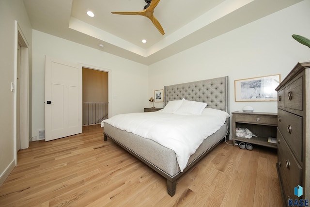 bedroom featuring ceiling fan, light hardwood / wood-style flooring, and a tray ceiling