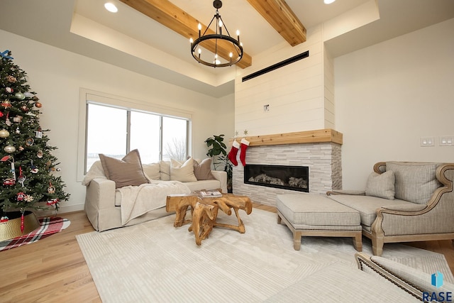 living room with a tiled fireplace, beamed ceiling, light hardwood / wood-style floors, and an inviting chandelier