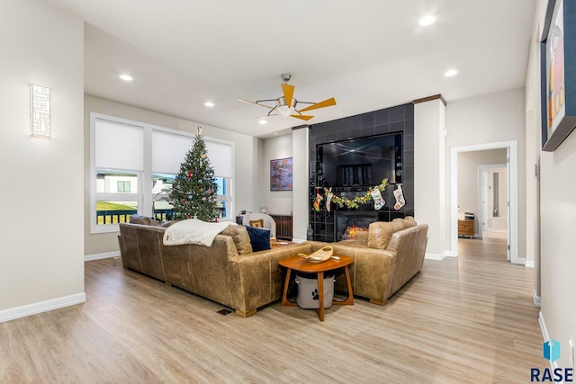 living room with light hardwood / wood-style flooring, ceiling fan, and a tiled fireplace