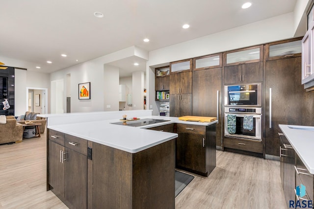 kitchen with black electric stovetop, dark brown cabinets, stainless steel double oven, a center island, and light hardwood / wood-style floors