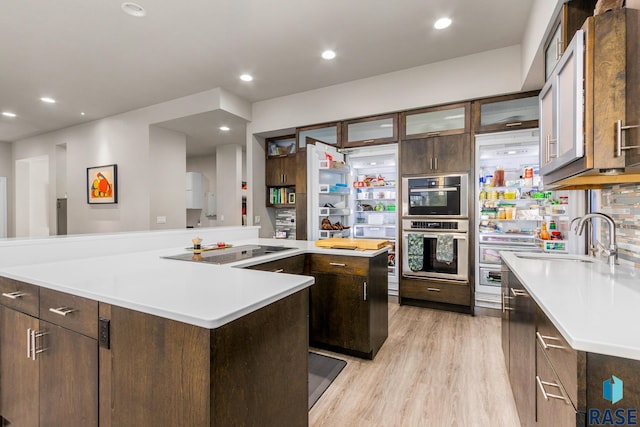 kitchen featuring sink, light hardwood / wood-style floors, black electric cooktop, dark brown cabinets, and a kitchen island