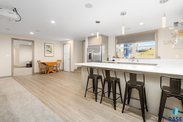 kitchen with stainless steel fridge, light hardwood / wood-style floors, a kitchen breakfast bar, and pendant lighting