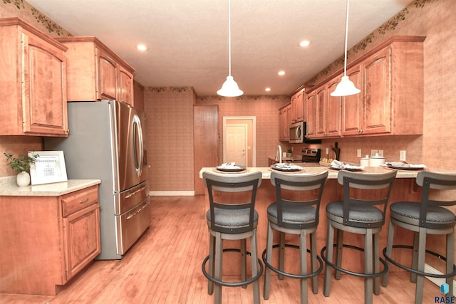 kitchen featuring stainless steel appliances, pendant lighting, and light wood-type flooring