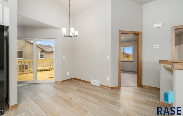 unfurnished dining area with a wealth of natural light, a towering ceiling, light hardwood / wood-style floors, and a notable chandelier