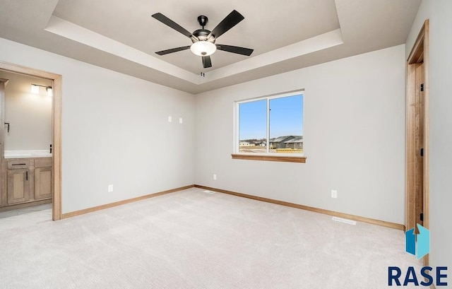 unfurnished bedroom with ceiling fan, a raised ceiling, light colored carpet, and ensuite bathroom