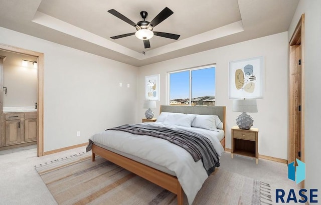 bedroom with a raised ceiling, connected bathroom, ceiling fan, and light carpet