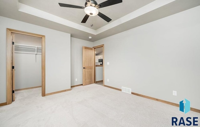 unfurnished bedroom featuring ceiling fan, light carpet, a tray ceiling, and a closet