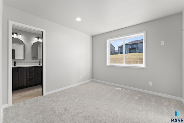 unfurnished bedroom featuring ensuite bathroom, light colored carpet, and sink