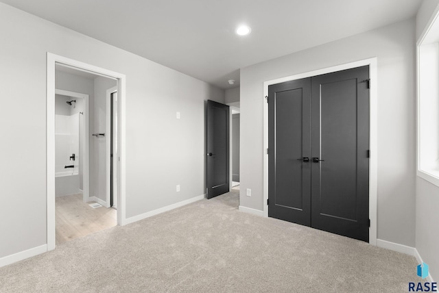 unfurnished bedroom featuring ensuite bath, a closet, and light colored carpet