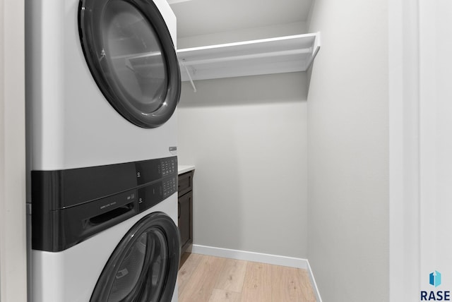 laundry area featuring cabinets, light wood-type flooring, and stacked washer / dryer