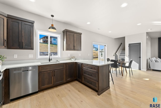 kitchen with kitchen peninsula, light wood-type flooring, sink, pendant lighting, and dishwasher