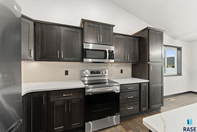 kitchen with appliances with stainless steel finishes, tasteful backsplash, dark brown cabinets, dark wood-type flooring, and lofted ceiling