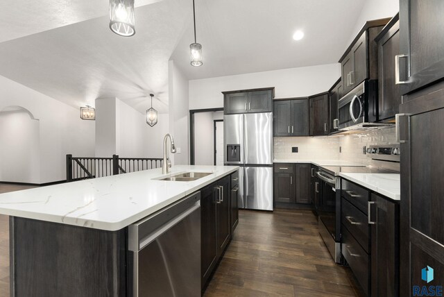 kitchen with sink, hanging light fixtures, dark wood-type flooring, stainless steel appliances, and a kitchen island with sink