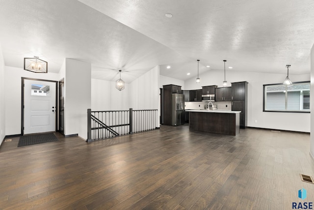 kitchen featuring hanging light fixtures, vaulted ceiling, dark hardwood / wood-style floors, an island with sink, and appliances with stainless steel finishes