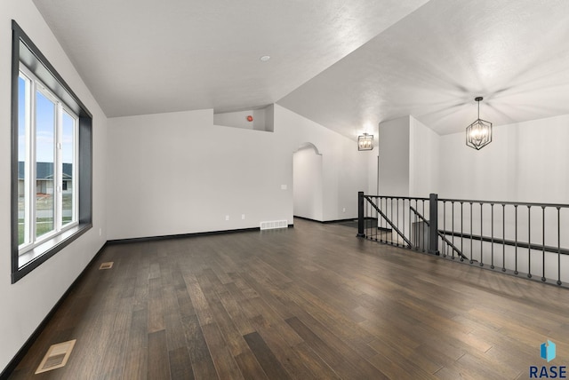 empty room with a chandelier, dark wood-type flooring, and vaulted ceiling