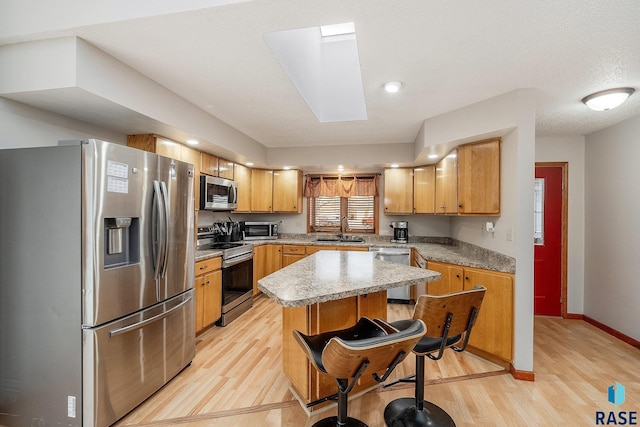 kitchen with sink, a skylight, a kitchen island, appliances with stainless steel finishes, and light hardwood / wood-style floors