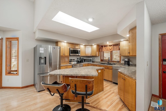 kitchen featuring a skylight, light hardwood / wood-style flooring, a textured ceiling, a kitchen island, and appliances with stainless steel finishes