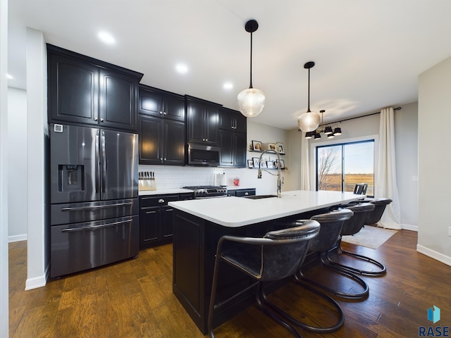 kitchen with stainless steel appliances, dark hardwood / wood-style floors, backsplash, an island with sink, and pendant lighting