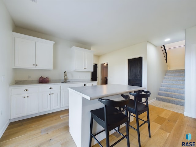 kitchen featuring a kitchen bar, light hardwood / wood-style floors, a kitchen island, and white cabinetry