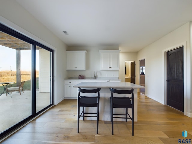 kitchen featuring a center island, sink, a kitchen breakfast bar, light hardwood / wood-style flooring, and white cabinets