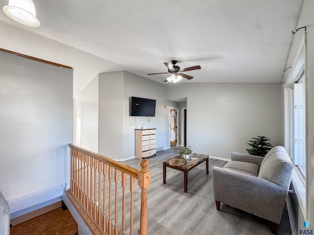 living room with a textured ceiling, ceiling fan, vaulted ceiling, and light wood-type flooring