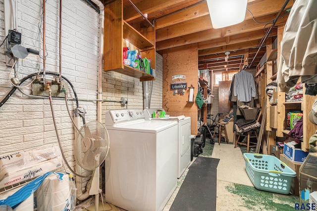 clothes washing area featuring independent washer and dryer and brick wall