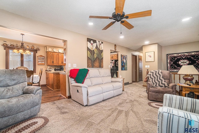 living room featuring light carpet, ceiling fan with notable chandelier, and a textured ceiling