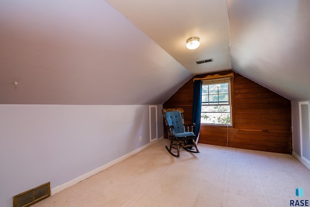 additional living space with wood walls, light colored carpet, and lofted ceiling