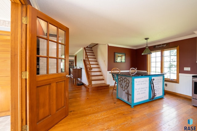 kitchen with light hardwood / wood-style floors, ornamental molding, hanging light fixtures, and stainless steel stove