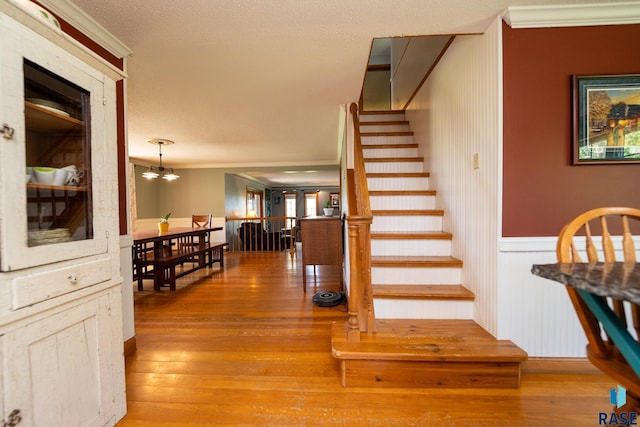 staircase featuring wood-type flooring, a textured ceiling, ornamental molding, and a notable chandelier