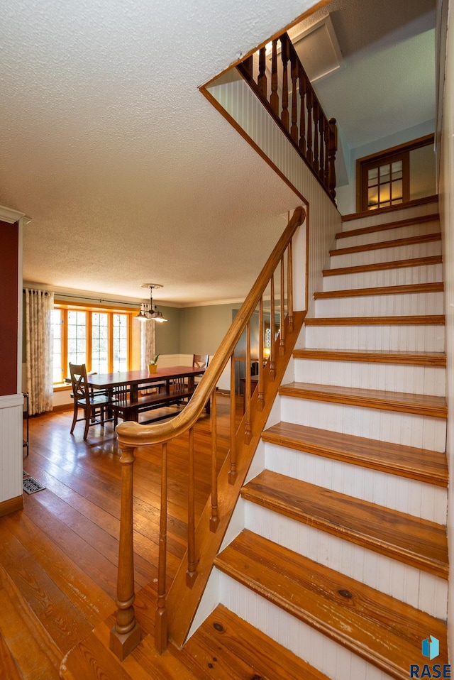 staircase with hardwood / wood-style floors, a textured ceiling, and an inviting chandelier