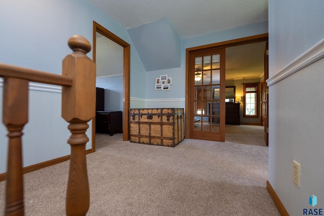 hallway featuring a textured ceiling, lofted ceiling, light carpet, and french doors