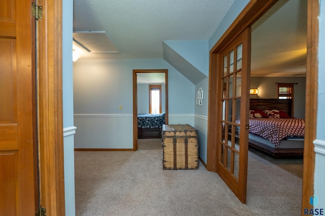 hall featuring a textured ceiling, light carpet, and vaulted ceiling