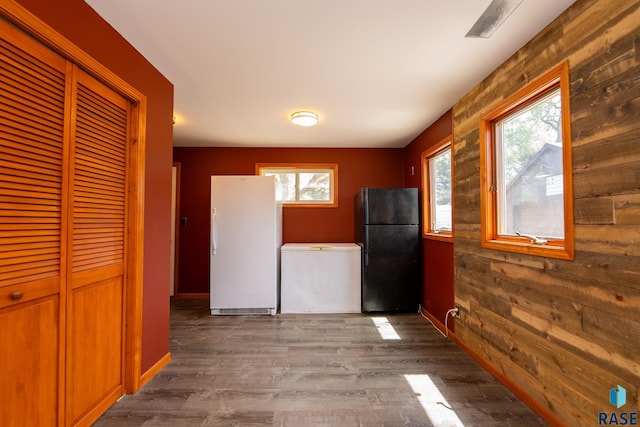 kitchen with black fridge, hardwood / wood-style floors, white fridge, and wood walls