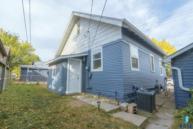 rear view of house with central air condition unit and a lawn