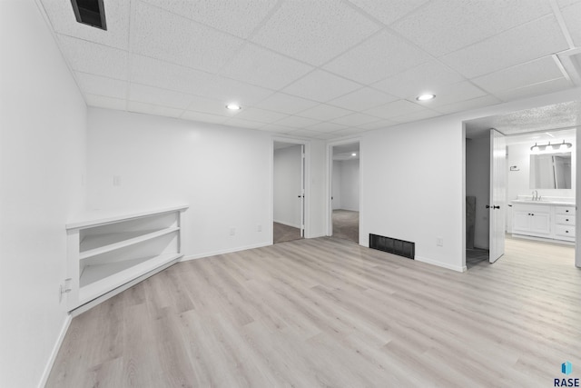 basement featuring a paneled ceiling and light hardwood / wood-style floors