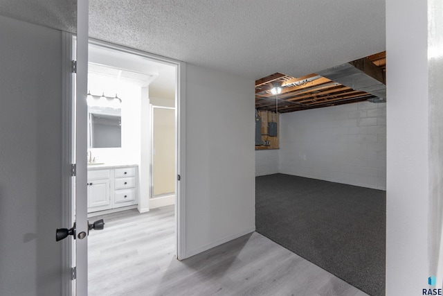 basement with sink, light wood-type flooring, and a textured ceiling