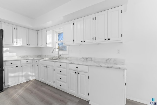 kitchen with light stone counters, light hardwood / wood-style flooring, white cabinetry, and sink