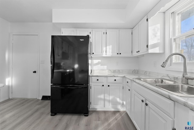 kitchen with white cabinets, light hardwood / wood-style floors, and black fridge