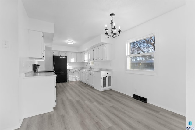 kitchen with white cabinets, black refrigerator, an inviting chandelier, and light hardwood / wood-style flooring