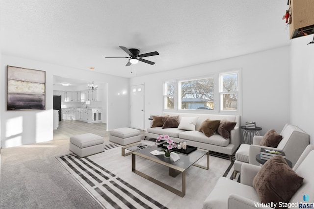 living room featuring sink, ceiling fan with notable chandelier, light colored carpet, and a textured ceiling