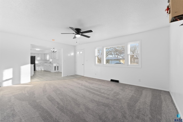 unfurnished living room with ceiling fan with notable chandelier, light colored carpet, and a textured ceiling