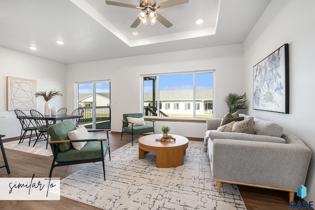 living room with a raised ceiling, ceiling fan, and light hardwood / wood-style floors