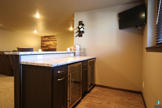 bar with dark brown cabinets, light hardwood / wood-style floors, light stone counters, and beverage cooler